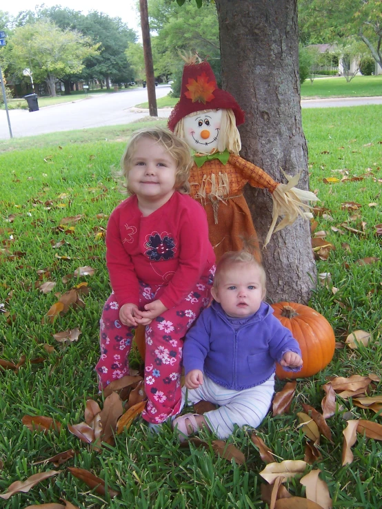two small children sitting under a tree near a pumpkin