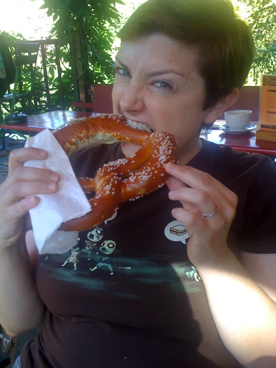 there is a woman eating a large pretzel at the table