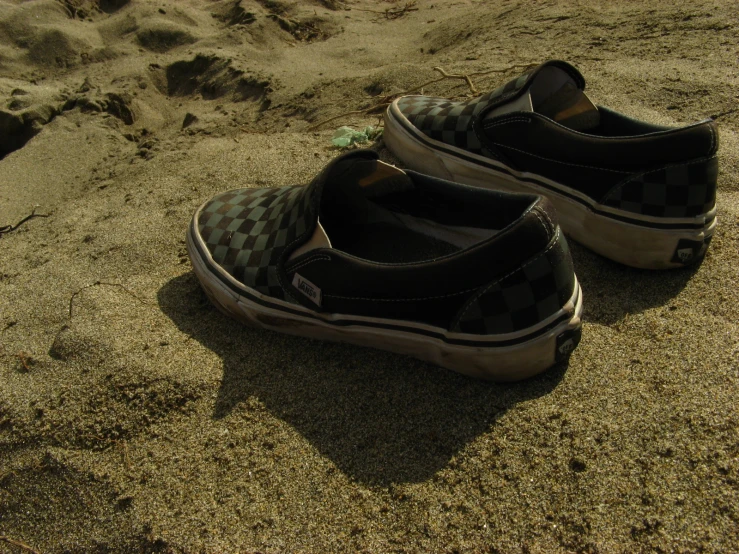 pair of vans in sand, with shoes next to them