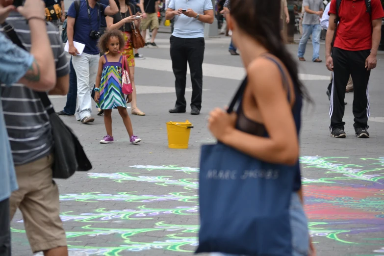 a girl is walking on the sidewalk while using chalk to draw