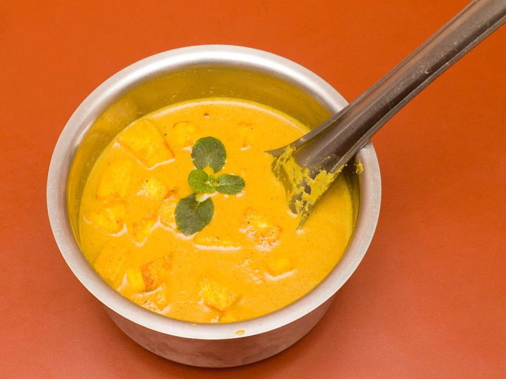 the bowl is full of orange soup with some basil