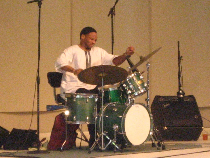 a drummer in white sits behind his drum kit