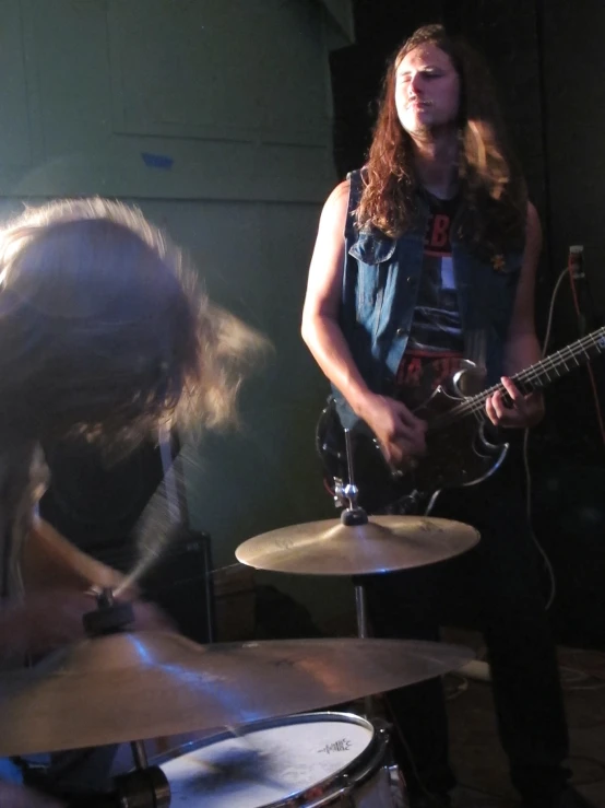 a man playing drums while another woman looks at the camera
