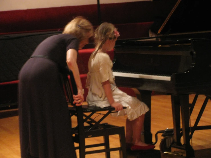 two women are sitting at a piano in an auditorium