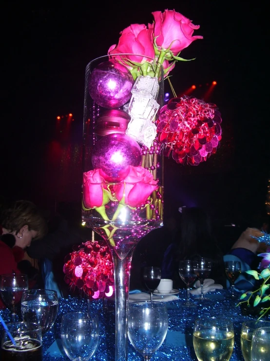 a group of roses in a vase with light up ornaments and wine glasses