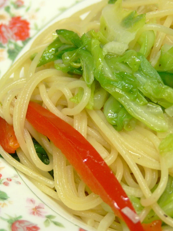 a plate with pasta and greens sits on a flowered cloth