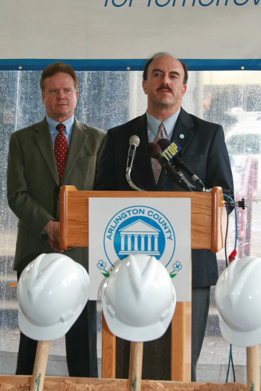 two men at a podium holding a construction helmet