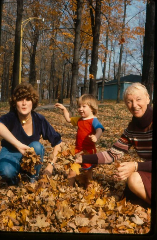 two ladies and a boy playing in some leaves