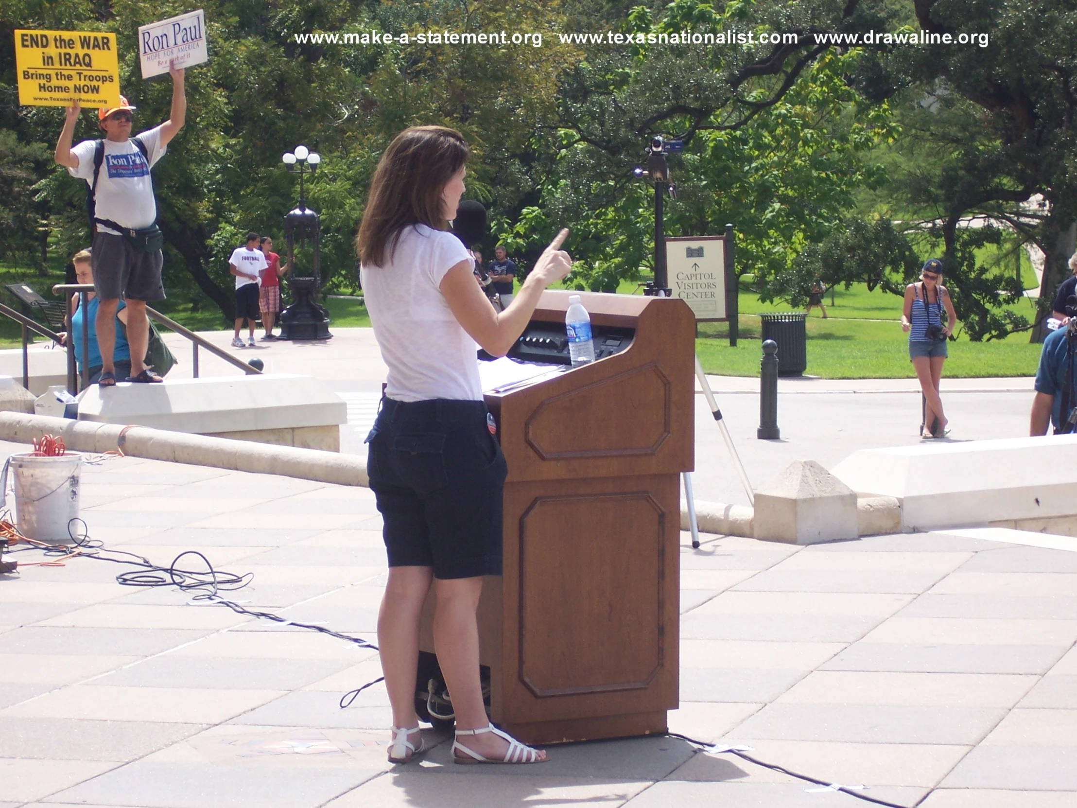 a woman with her hands up behind a podium on the sidewalk