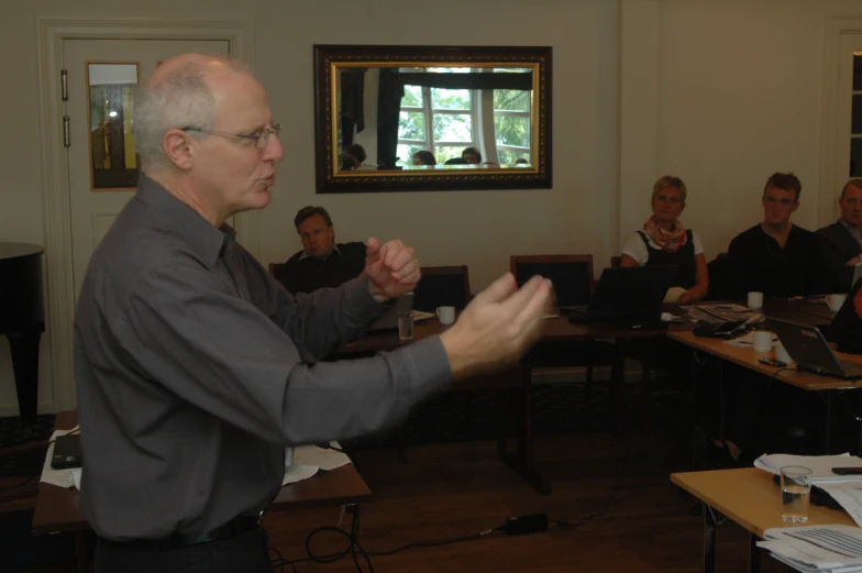 a man standing in front of people while wearing glasses