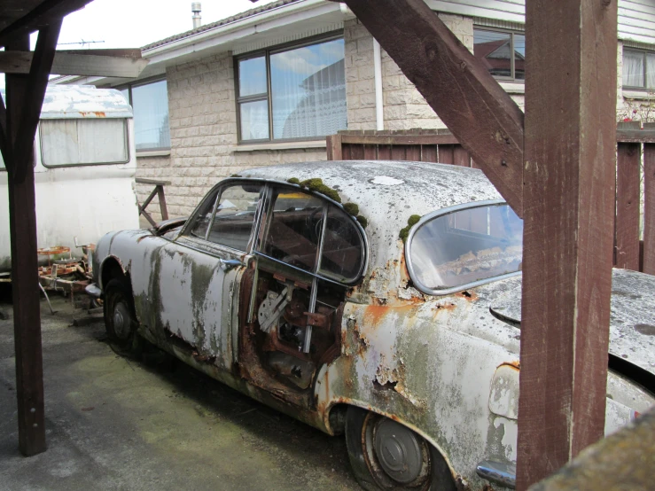 the old car is sitting rusty outside of a home