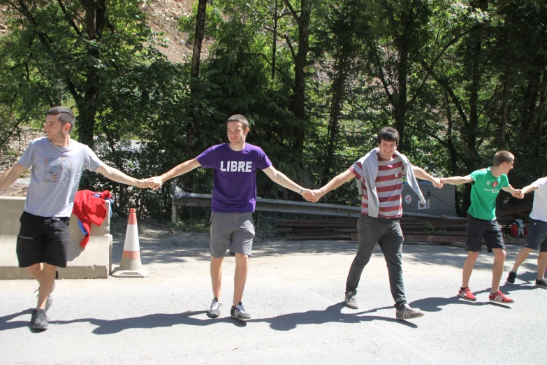 four young men hold hands while walking through the park