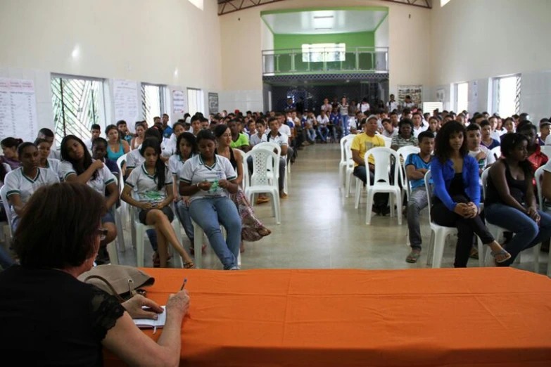 large group of people sitting in white chairs listening to a lecture