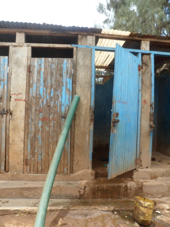 this is a very dirty looking building with doors and a green hose in front of it