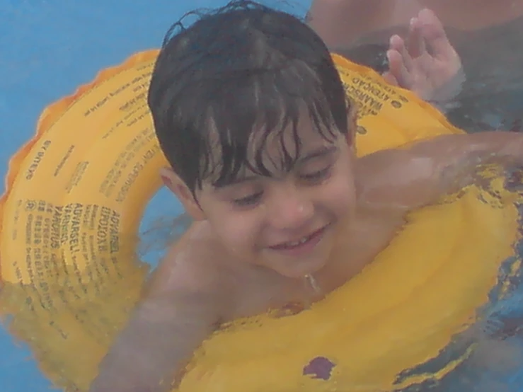 a boy in a yellow life jacket swims with his arm around a float ring