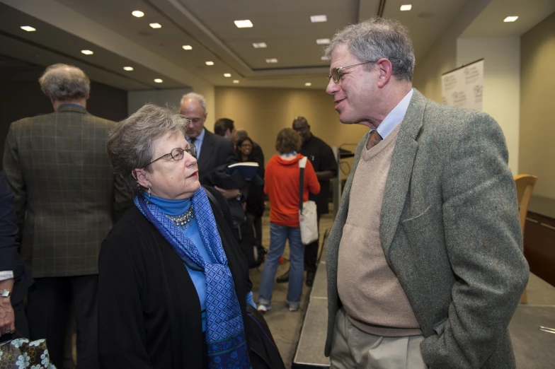 a man talking to an older woman in a room full of people