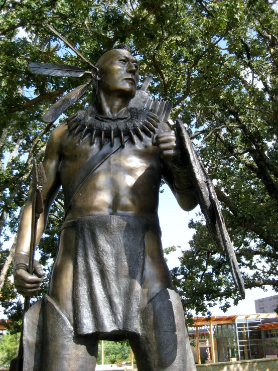a statue is near a park setting, where a man holds a spear and talks