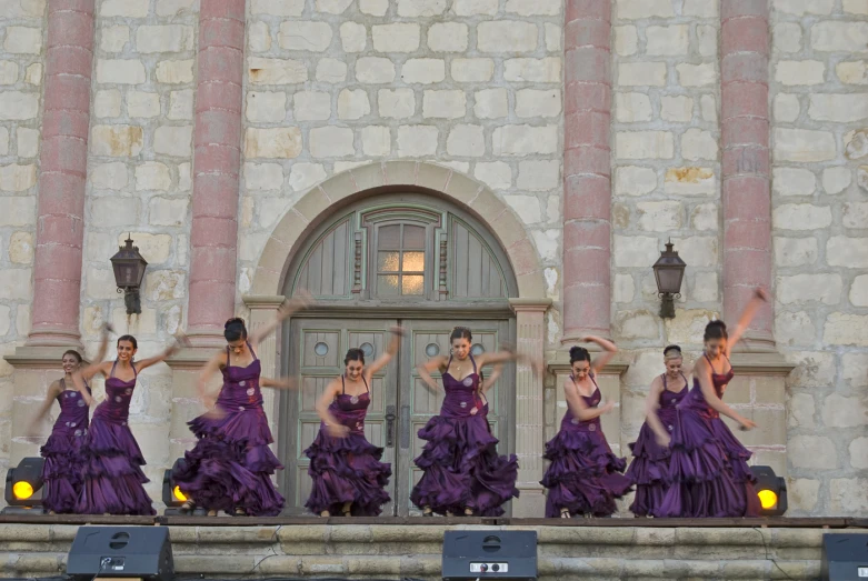 women wearing long purple dresses on stage in front of a building