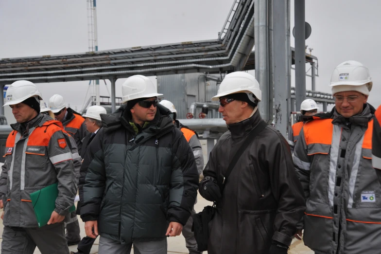 a group of men wearing hard hats in front of a large factory