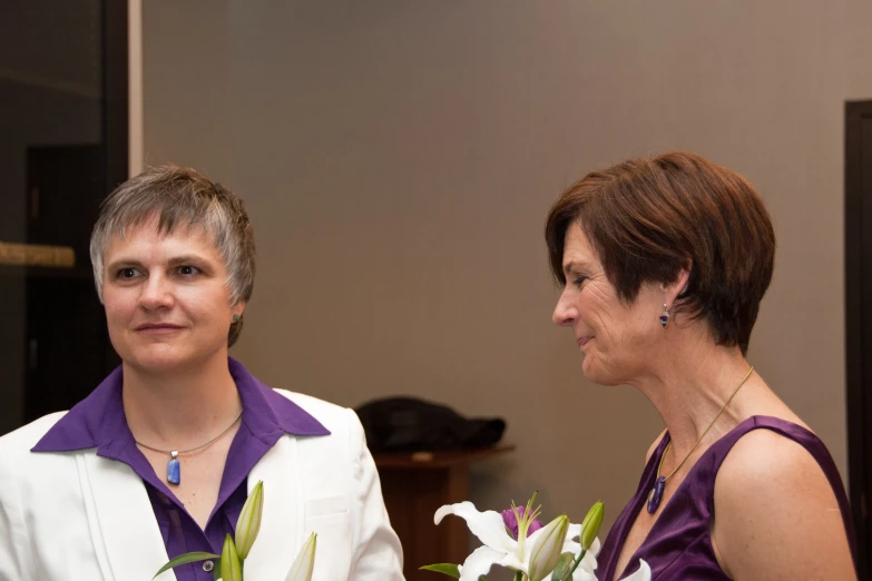 two women smile while one holds flowers and the other looks away