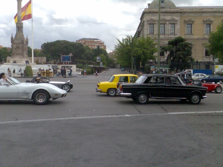 some old cars driving down the street with buildings in the background