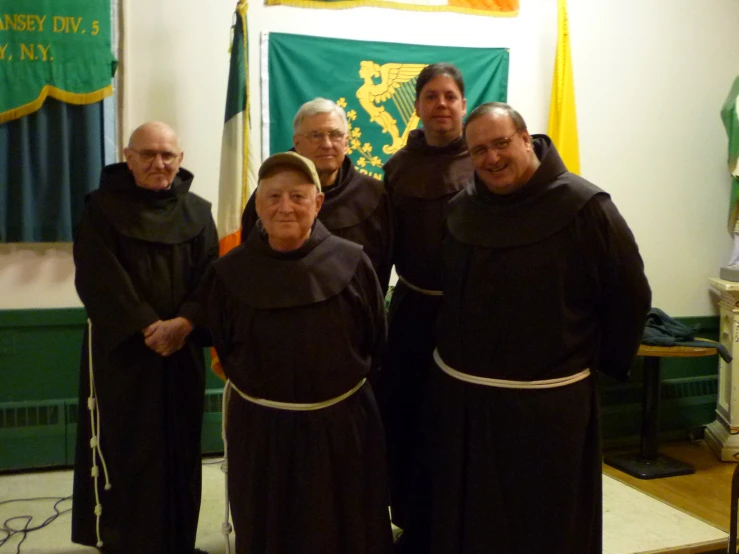 two groups of men and one woman in black robes stand in front of a large flag