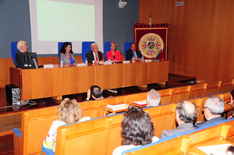 a group of people sit in front of rows of chairs as the panel looks on