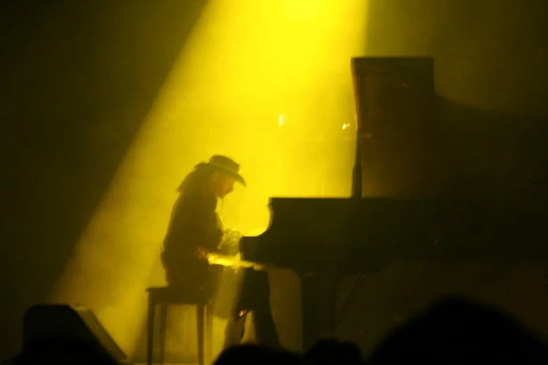 the man is sitting at a piano as the light shines behind him