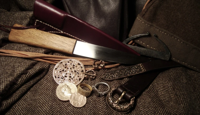 a long knife, several pieces of chain and two celets are laying on some cloth