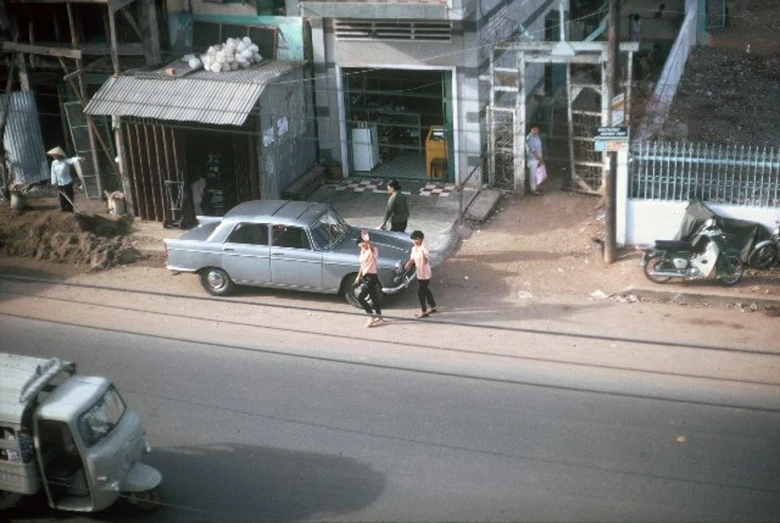 two people crossing a street with cars and people walking on the side