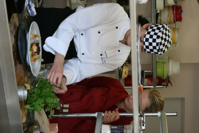 two women in chefs uniforms cooking vegetables on a plate