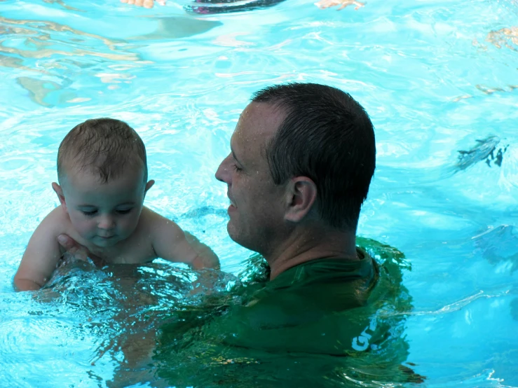 an adult in the pool with a child looking at him