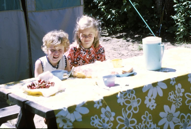 two children sitting at an outdoor table with plates of food on it