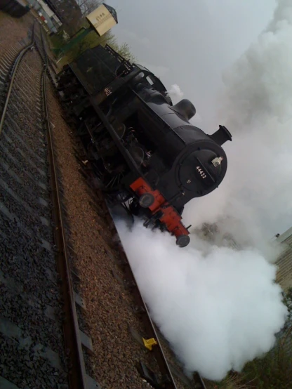 a black and red train pulling a train track with steam pouring out