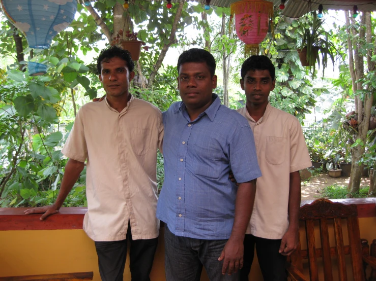 three men in shirts stand together near a bench