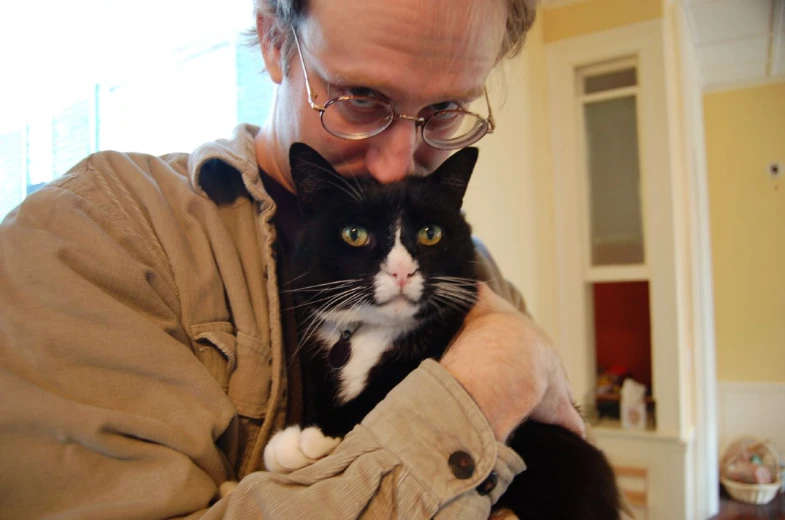 a man in glasses holding a cat in his arms