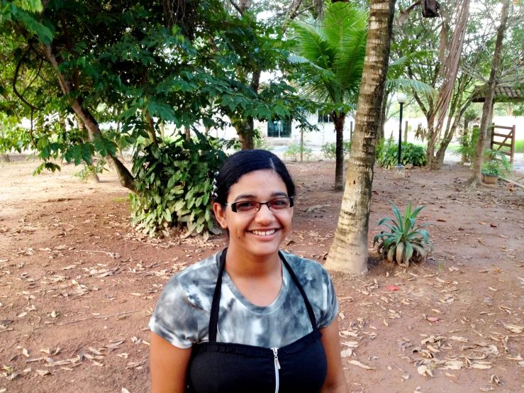 a woman wearing an apron poses in front of some trees