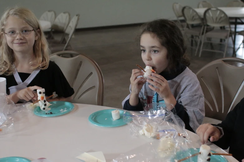 two children are sitting at a table eating cake