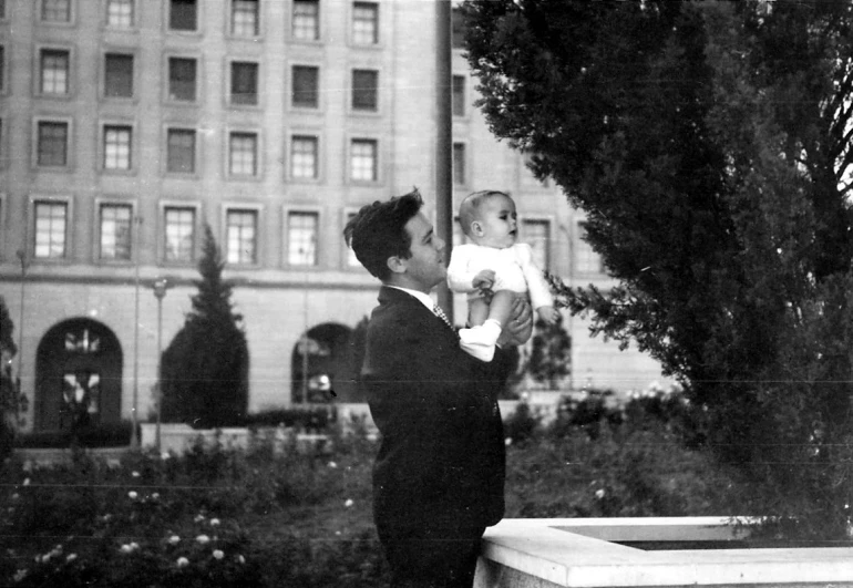 a woman standing on top of a lush green field holding a baby