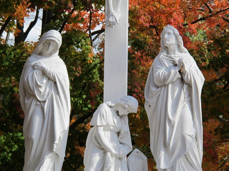 three white sculptures stand in front of a green leaf filled tree