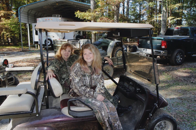 two women sit on a golf cart near the back of a truck