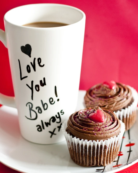 two cupcakes on a plate near a coffee mug