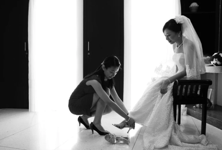 a bride putting on shoes as another puts on her dress