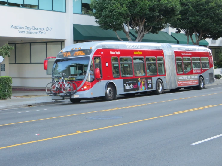 a red and silver bus on the side of a road with buildings in background