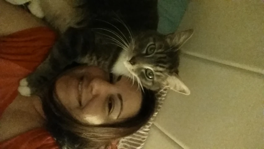 a woman smiles with a cat perched on her head