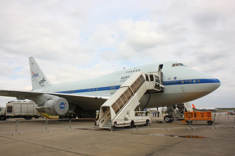 an airplane parked at an airport while people wait on the stairs