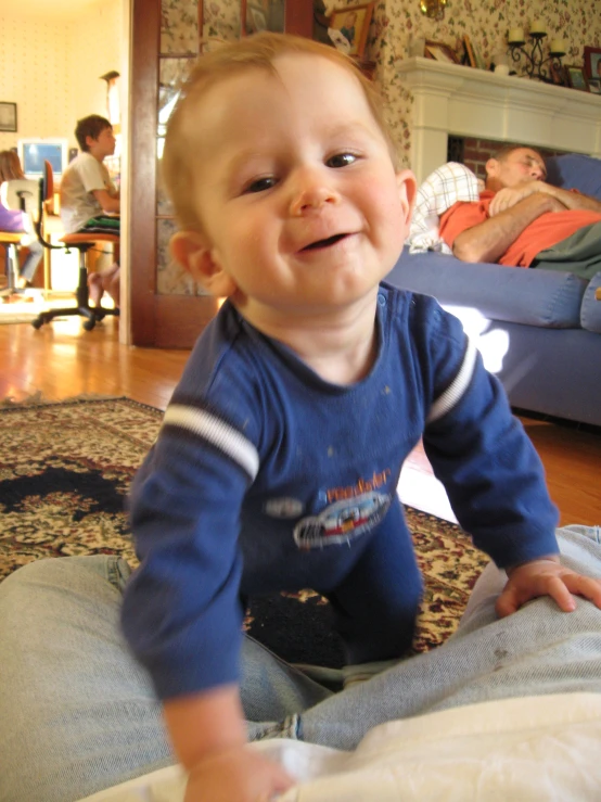 a smiling baby holding a wii mote while sitting on the floor