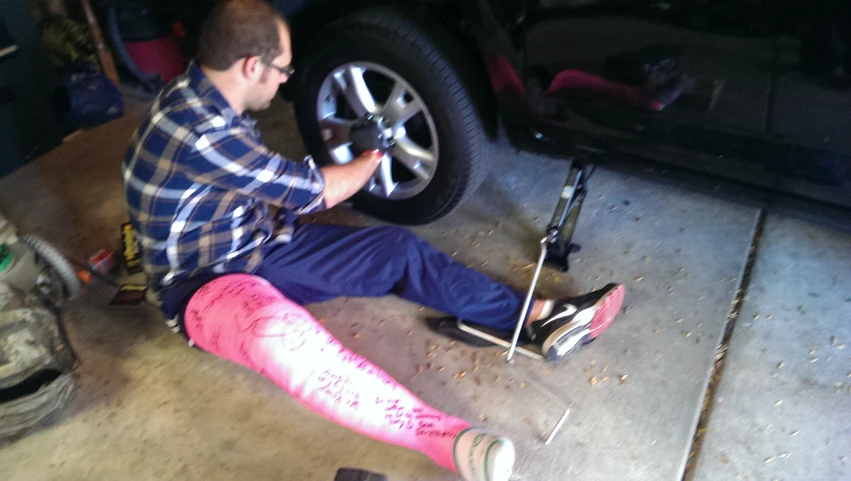 man with skis working on a tire while wearing pink leggings