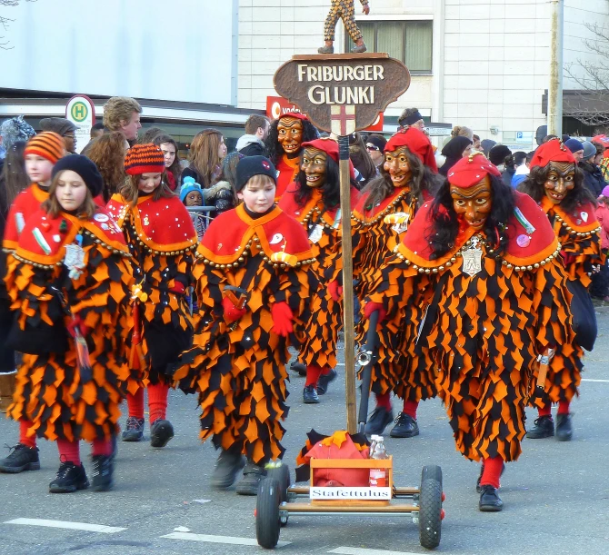 a group of young people dressed in orange and black costume marching through the street