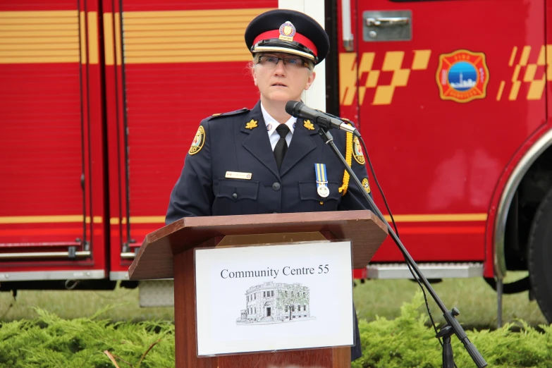 a woman in military uniform stands at a podium near fire engines